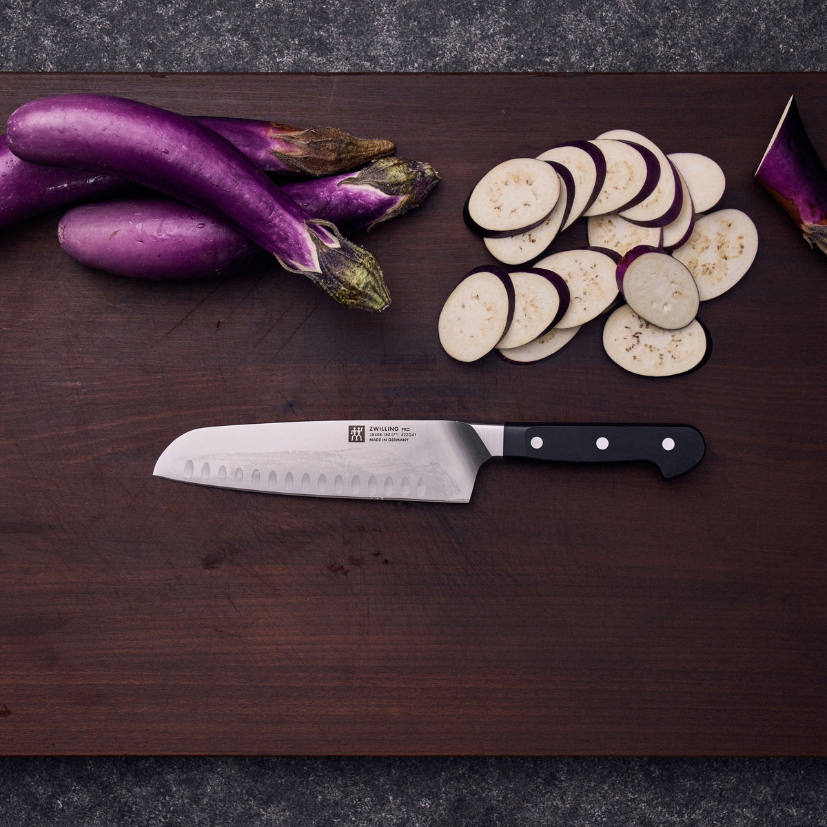 Het santokumes met kuiltjes van bovenaf naast gesneden aubergine op een donkere plank