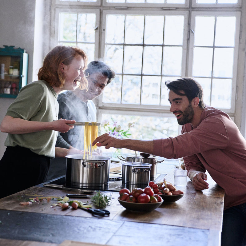 Drie mensen koken samen aan een houten tafel met pannen van Zwilling